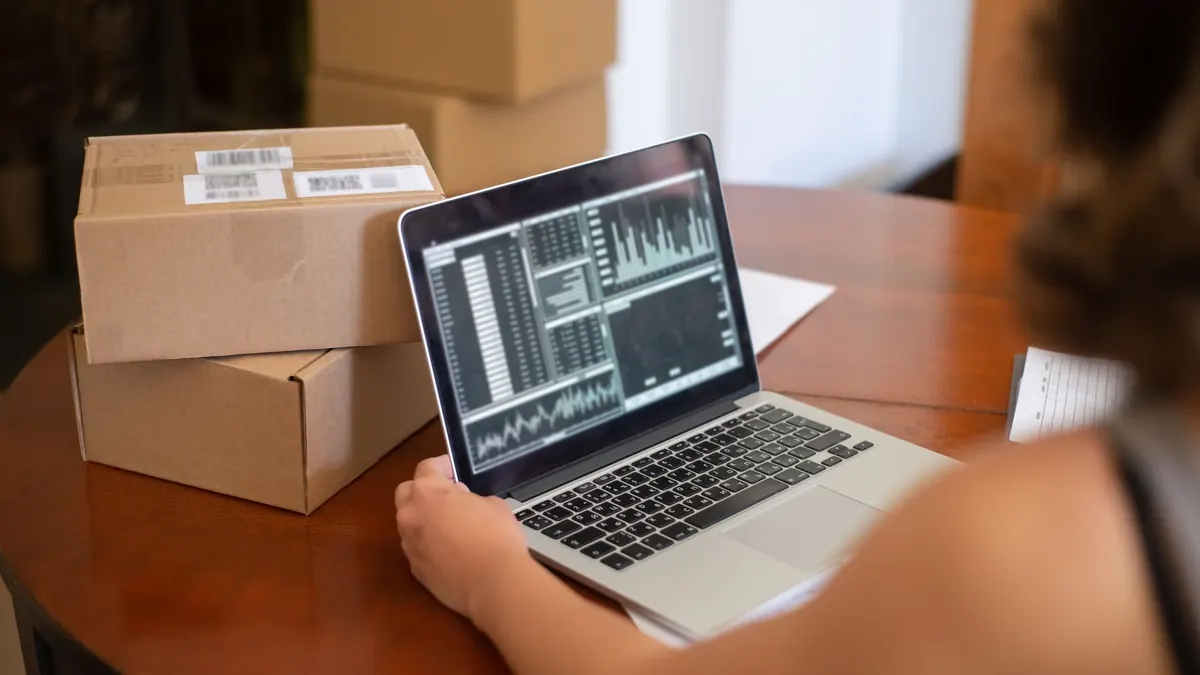 Portátil con cifras de ventas junto a cajas de envío al comparar tienda online o web a medida