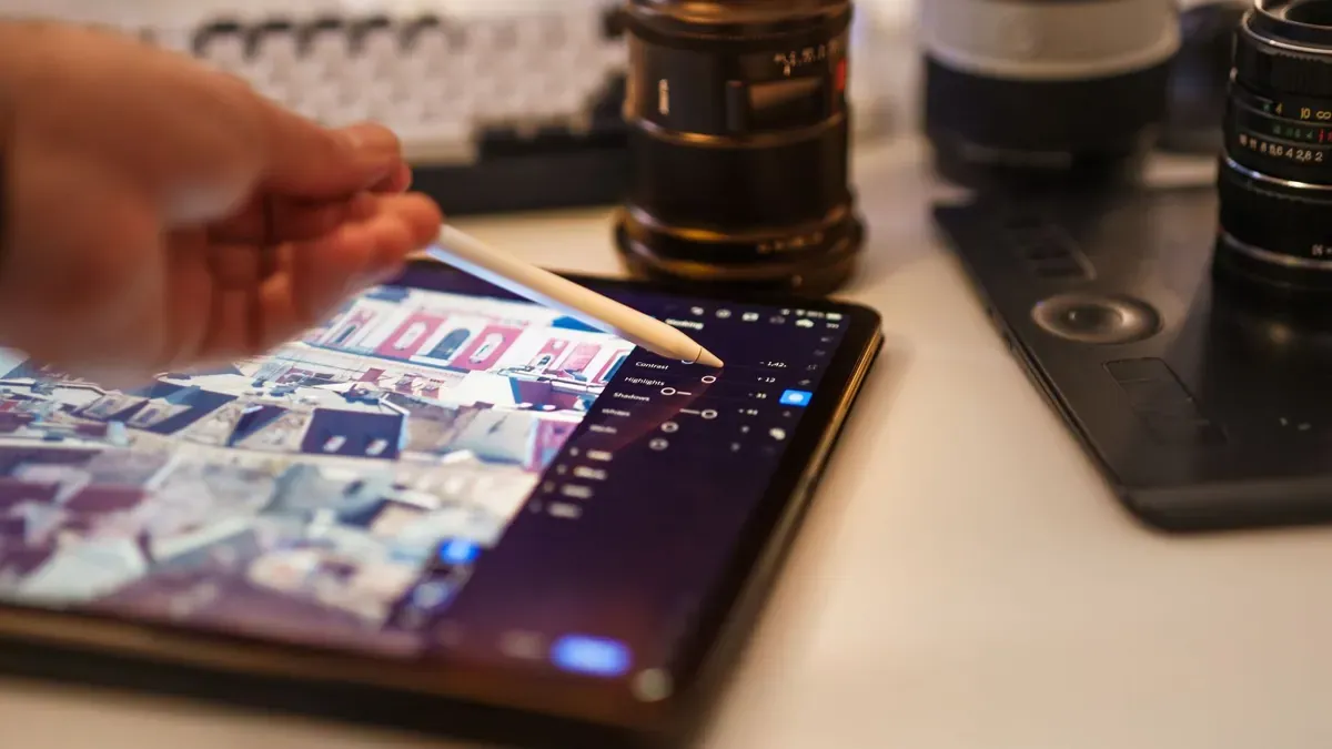 Manos retocando fotografías en una tableta junto a varios objetivos de cámara