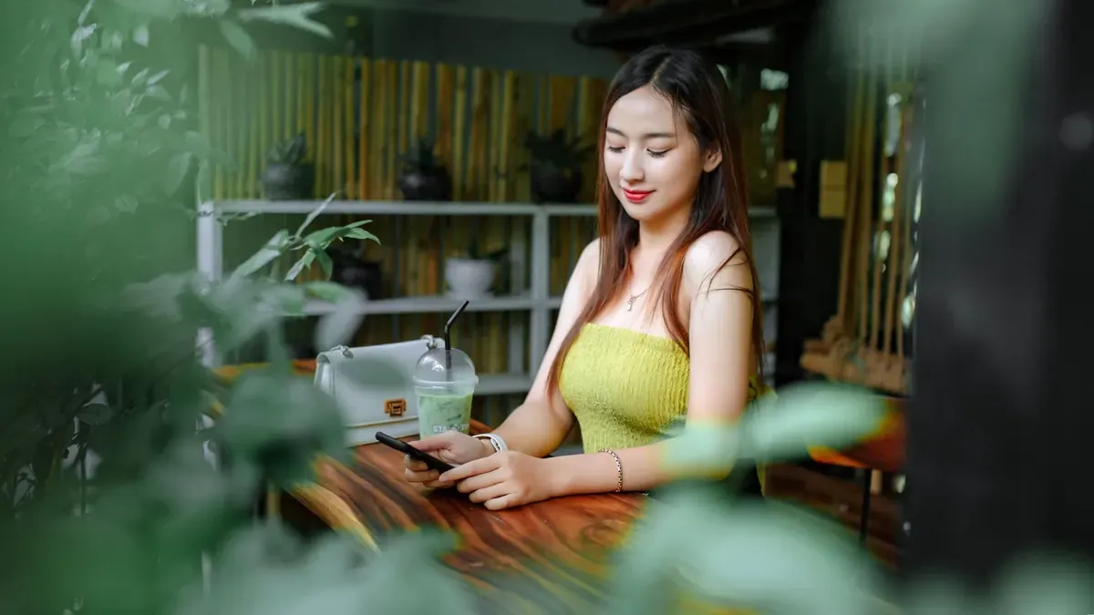 Mujer mirando el móvil en una cafetería rodeada de plantas