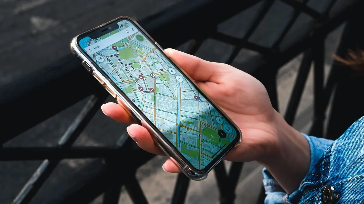 Una mano sostiene un móvil con el mapa abierto en plena calle, como quien busca un negocio cercano en Google